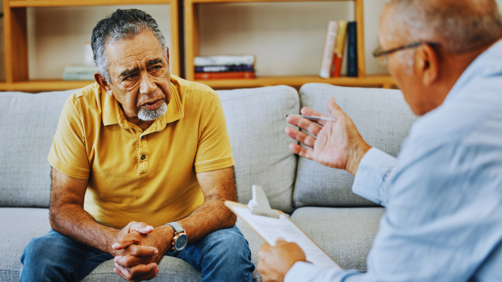 An older adult smiling while talking with a mental health therapist in a comfortable office setting.