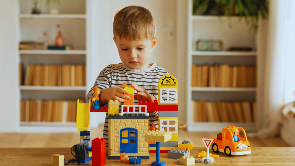 A young child sits on the floor, arranging colorful building blocks, with a soft-focus background of a therapy room.