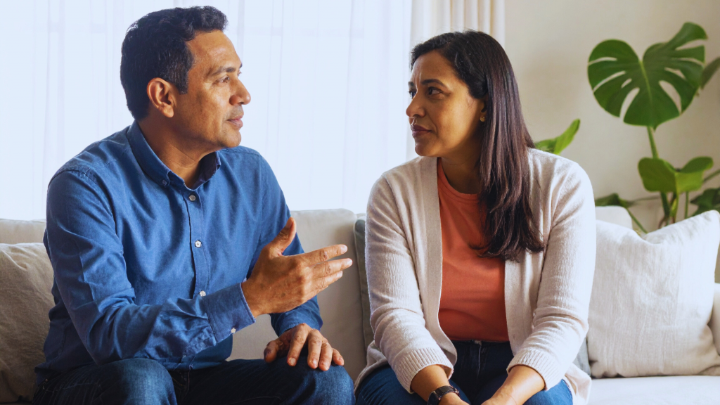 Couple sitting together having a calm conversation on a comfortable couch, representing healthy communication during difficult times